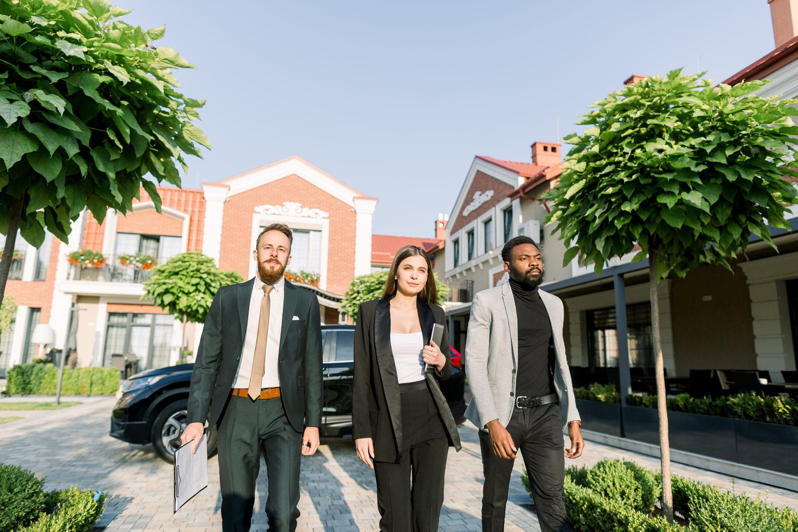 Elegant businesspeople, African and Caucasian man, Caucasian woman, walking outdoors on the yard of modern office business center